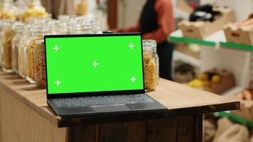 Computer showing blank chromakey display next to goods in jars, local grocery store supporting organic farming and sustainable lifestyle. Modern laptop running greenscreen isolated layout. Camera A. video