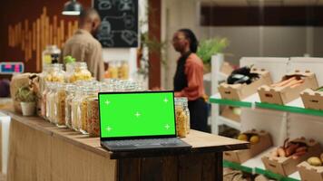 Laptop auf Stall beim Supermarkt zeigen grüner Bildschirm Vorlage, Menschen Einkaufen zum organisch einheimisch Produkte im Null Abfall Öko speichern. tragbar pc mit leer Chromakey und Exemplar. Kamera a. video