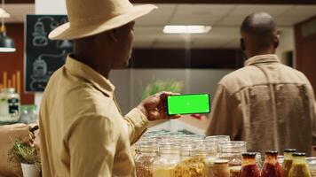 petit affaires propriétaire les usages écran vert disposition sur téléphone intelligent application, en présentant isolé afficher avec fond modèle. local agriculteur en portant téléphone avec Vide maquette chromakey écran dans magasin. caméra un. video