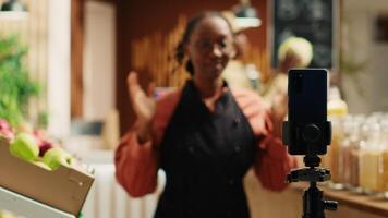 African american vendor presenting variety of pasta in jars, discussing about ethically sourced products and homemade food alternatives. Filming promotional video for healthy lifestyle. Camera A.