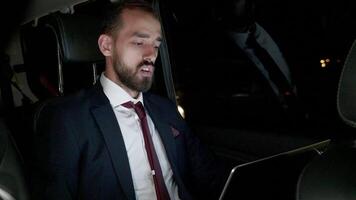 Businessman having a video conference with his business partner sitting in the back seat of his limousine with personal driver.