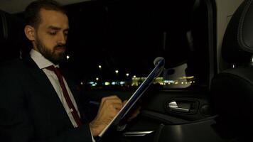 Vorsitzender im Geschäft passen nehmen ein Selfie im das zurück von seine Limousine und Arbeiten auf seine Tablette beim Nacht. Geschäftsmann im Anzug. video