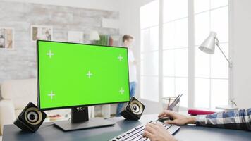 Zoom out footage of male typing on keyboard of a green screen PC display in well lit living room video