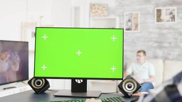 Man working on green screen PC display in bright and modern flat while his roommate watches TV in the background video