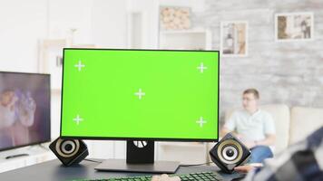 Man working on green screen PC display in bright and modern flat while his roommate watches TV in the background video