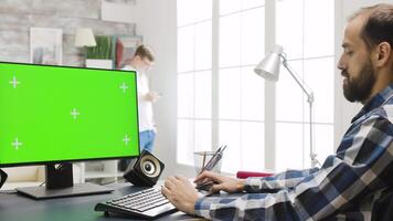 persona trabajando en ordenador personal monitor con verde pantalla en acogedor brillante vivo habitación. en el fondo - un persona es mirando a su teléfono video
