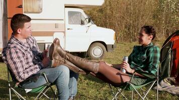 Caucasian copuple relaxing together on camping chairs in front of their retro camper van. video