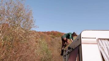 Beautiful caucasian young woman getting down from the top of her camper van while her boyfriend is helping her. video