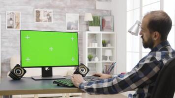 Mens werken Aan groen scherm pc in helder kamer Bij huis. in de achtergrond - goed lit leven kamer en een Mens aan het kijken de TV video