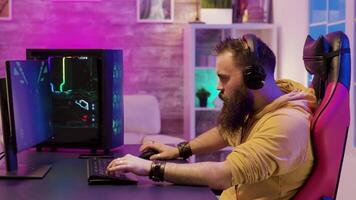 Professional game player wearing headphones in a room with colorful neons while playing online video games.