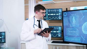 médico en un moderno neurociencia centrar haciendo notas en tableta. paciente vistiendo ondas cerebrales exploración centro. video