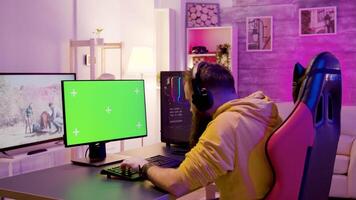 Mens in zijn kamer ontspannende spelen video spellen Aan computer met groen scherm. Mens zittend Aan gaming stoel.