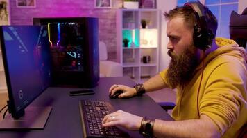 Bearded hipster chatting and playing a shooter game on his powerful PC with RGB lighting in neon colored room video