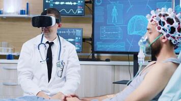 Doctor in a neuroscience centre wearing a virtual reality goggles while patient is sleeping on hospital bed wearing brainwaves scanning headset and air mask. video