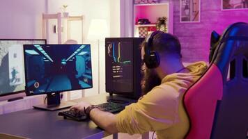 Bearded hipster man in a room with colorful neon lights sitting on gaming chair playing an online shooter game with his friends. video