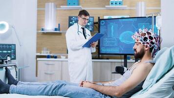 médico analisando paciente sentado em cama e vestindo cérebro digitalização dispositivo. paciente vestindo ondas cerebrais digitalização fone de ouvido. video