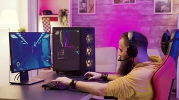 Bearded man playing online video games on his pc and talking with others players. Colorful neons in the room.