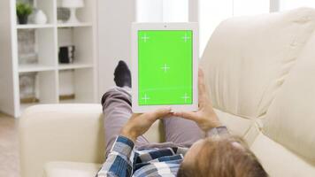 Young caucasian man holding a digital tablet PC with green screen on it. In the background - modern, well lit living space video