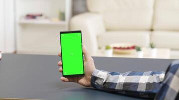 Zoom in parallax shot of man holding a green screen phone on the table in bright and well lit house video