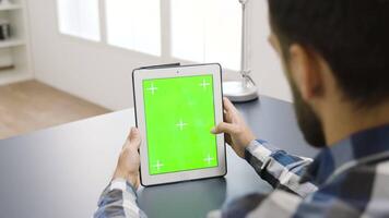 Man touching the screen of a digital tablet PC with green mock-up on it. In the background - well lit and bright living space video