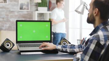 Over the shoulder parallax shot of man working on laptop with green screen in bright, well lit and modern living space video