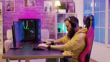 Man sitting on a gaming chair and playing video games in his room with colorful neons wearing headphones.