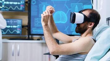 Patient with virtual reality goggles in a modern facility for brain research making hand gestures sitting on bed. video