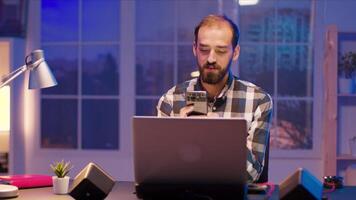 Young freelancer typing on his phone while having a video call. Freelancer working from home at late hours.