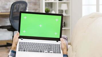 Zoom out parallax shot of man holding a green screen laptop lying on the couch in bright and well lit living space video