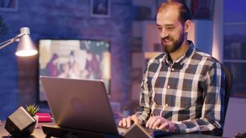 Bearded software engineer laughing while working late hours from home on laptop sitting at his desk. video