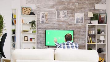 zurück Aussicht von jung Mann Aufpassen Sport auf Fernseher. Fernseher mit Grün Bildschirm. Mann entspannend auf Sofa tragen ein Shirt. video