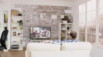 Back view of caucasian man relaxing on sofa and watching a movie on television video