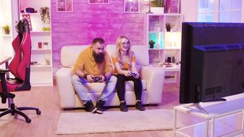 hermosa rubia hembra jugando en línea vídeo juegos juntos con su amigo sentado en sofá. video
