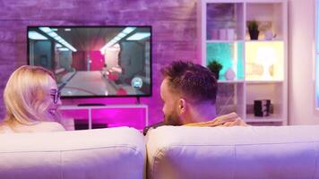 Best friends relaxing on couch and playing online video games using wireless controllers.