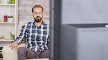 Bored caucasian man sitting on couch and watching tv while holding remote control. video