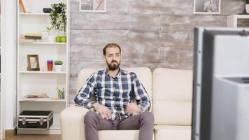 barbu homme avec curieuse expression tandis que en train de regarder la télé séance sur canapé dans le sien appartement. video