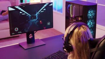 Cheerful young girl playing shooter games sitting on gaming chair in neon room video