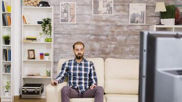 Bearded bored man watching television sitting on couch. Man holding tv remote control. video