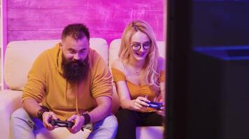 blond vrouw glimlachen terwijl spelen video spellen met haar vriendje gebruik makend van draadloze controllers Aan een groot scherm TV