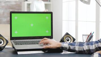 Man sitting at the desk in bright and well lit living room looking at laptop with green screen display. video