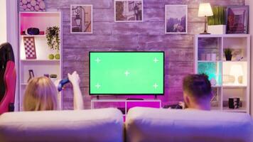 ung par Sammanträde på soffa och spelar uppkopplad spel på TV med grön skärm. Lycklig relation. spelare par. video