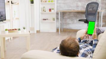 Parallax shot of male lying on the sofa and looking at green screen phone in well lit, bright living space video