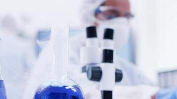 Close up of smoking blue fluid on lab bottle and scientist typing on laptop. Scientist in coverall equipment. video