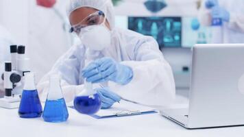 Female scientist in chemistry laboratory working with different smoking blue liquids. Team of scientist working in the background. video