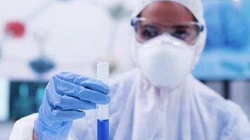 Woman scientist looking and holding a smoking blue fluid in a test tube. Team of scientist working in the background. video