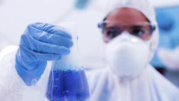 fechar acima do fêmea cientista dentro proteção equipamento segurando uma garrafa com fumar azul fluido. tóxico azul fluido com bolhas. video