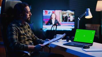 Teleworking financial advisor analyzing statistical charts on documents in front of green screen laptop in living room. Remote worker checking business paperwork, looking at mockup notebook video