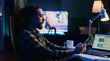 Man taking break from checking financial graphs on laptop, playing games on phone. Remote worker relaxing after analyzing business graphic figures, enjoying videogame on smartphone, camera A video