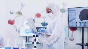 fêmea cientista trabalhando em computador caminhando dentro Ciência laboratório. cientista trabalhando dentro a fundo vestido acima dentro macacão equipamento. video