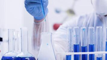 Female chemical scientist in a modern laboratory pouring reagent with pipette from test tubes with blue liquid. Scientist in modern laboratory. video